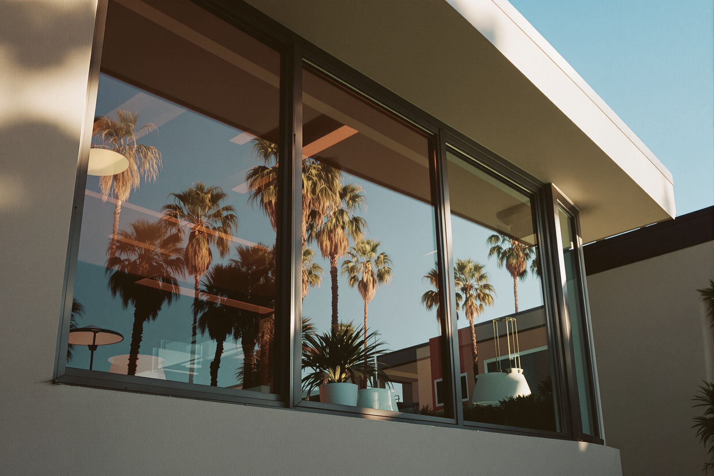 A California house front with dark tinted windows reflecting palms
